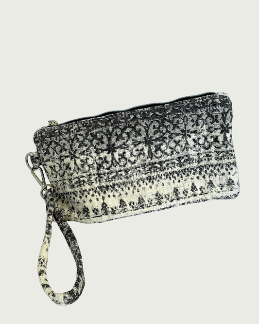 A wristlet in a gray and ivory fair isle-like print with a top zipper closure, gunmetal hardware, and and detachable wrist strap.