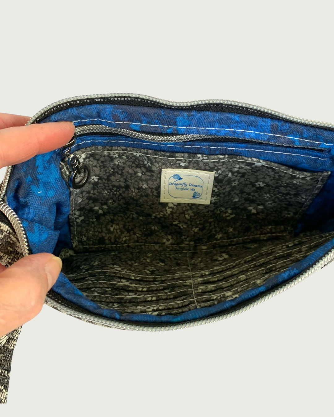 The interior of a handbag with sapphire blue and black lining and a black, gray, and white calico cardslot insert and zippered pocked.