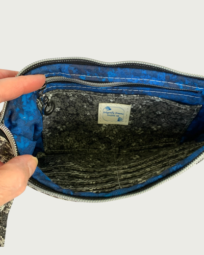 The interior of a handbag with sapphire blue and black lining and a black, gray, and white calico cardslot insert and zippered pocked.