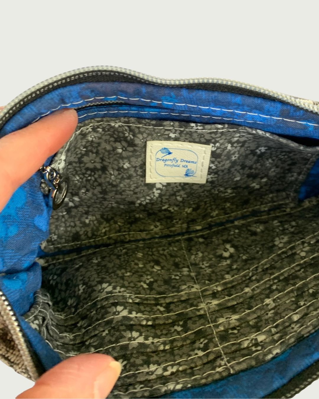 Close up of the interior of a handbag with sapphire blue and black lining and a black, gray, and white calico card-slot insert and zippered pocked.