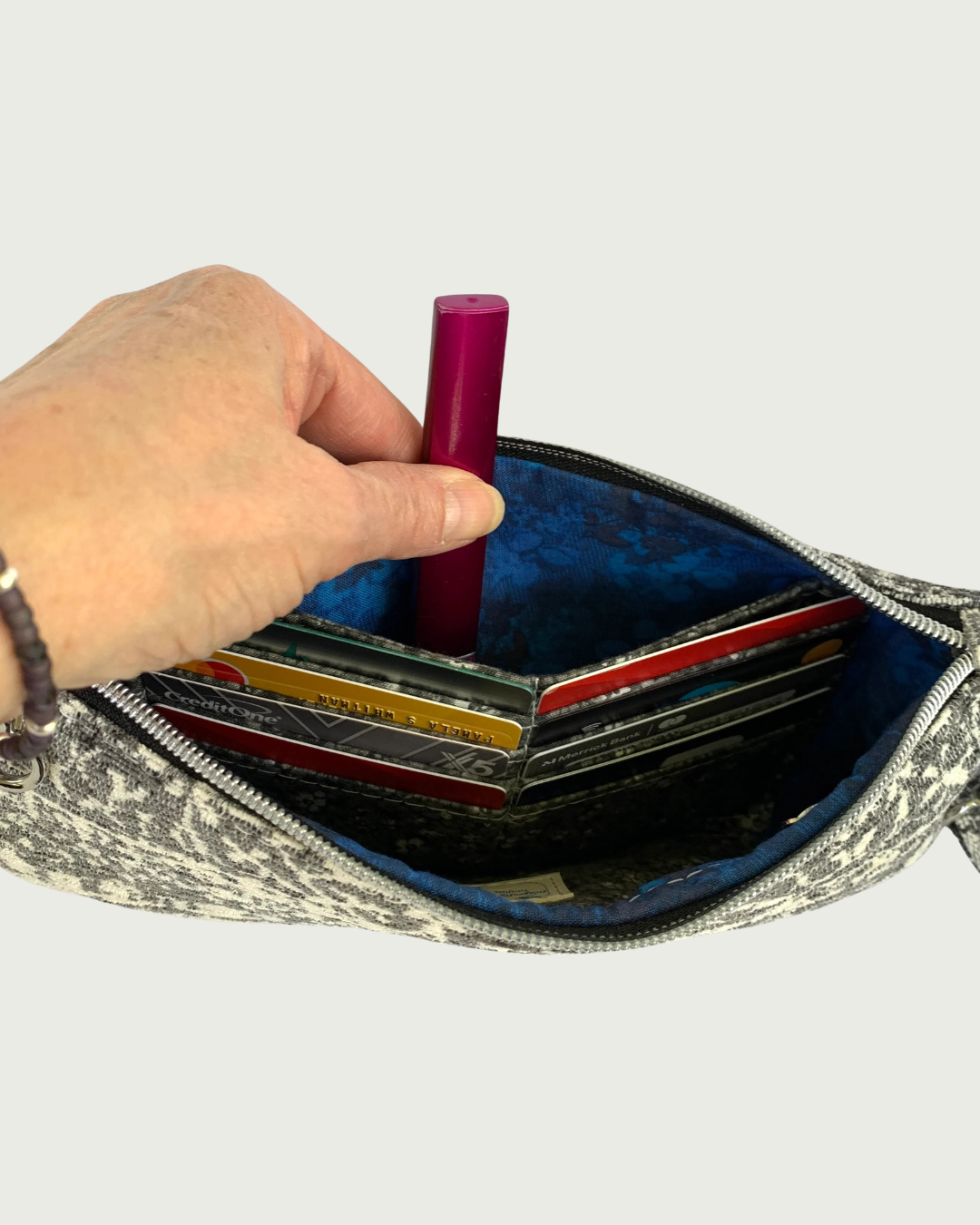 The interior of a handbag with sapphire blue and black lining , eight credit cards in slots, and a slip pocket.