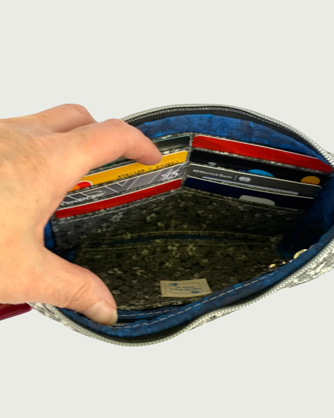 The interior of a handbag with sapphire blue and black lining , and a black, gray, and white calico card slot insert filled with eight credit cards. 