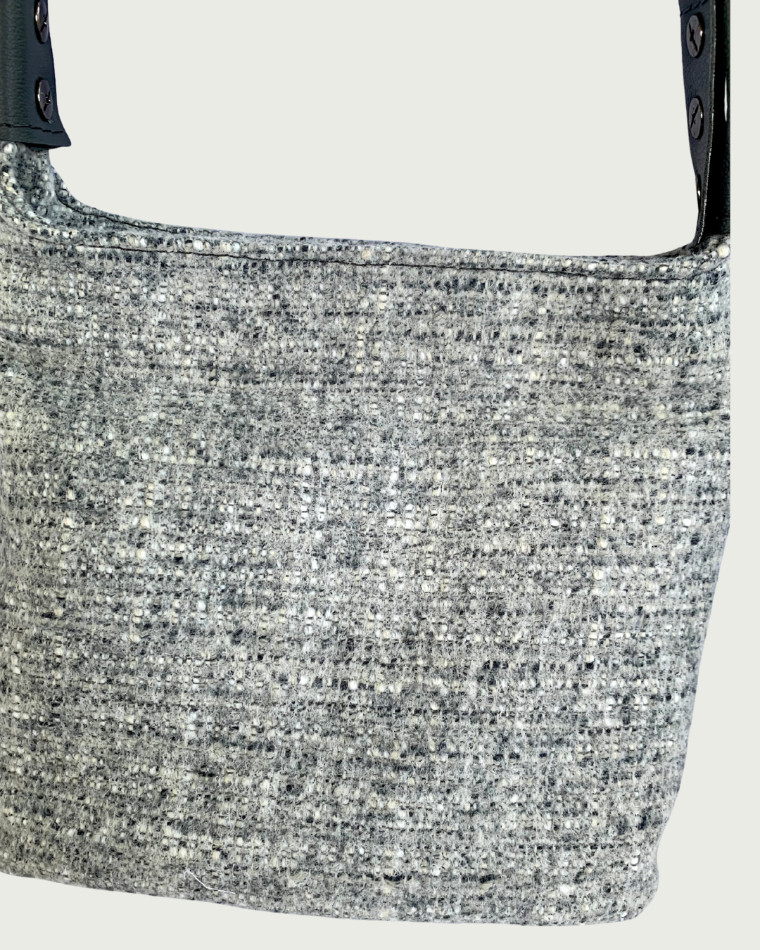 A closeup view of a gray wool-like handbag with gray vinyl strap connectors.