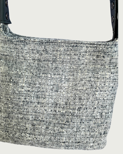 A closeup view of a gray wool-like handbag with gray vinyl strap connectors.