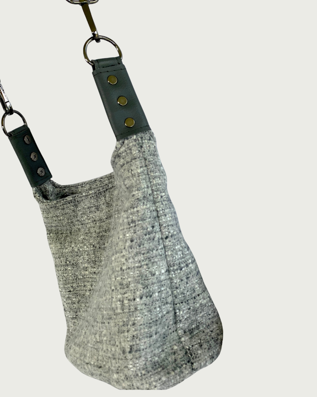 Gray wool-like slouchy shoulder bag with gray vinyl strap connectors as viewd from the side.