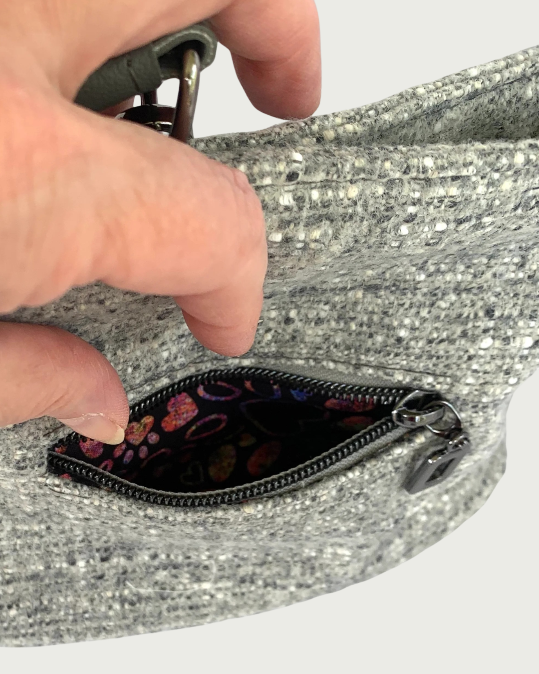 Close-up of a hand opening a zippered pocket on a textured gray fabric bag with a  multicolored interior lining.