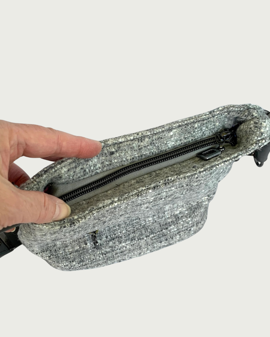Gray wool-like shoulder bag with gunmetal hardware as shown from the top recessed zipper.