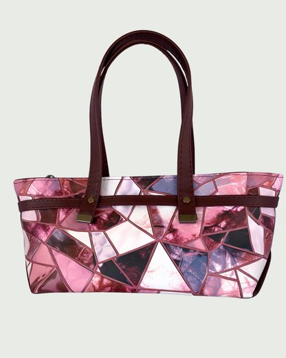Handmade East-West style bag made from vinyl in a print of fracture glass in colors of pink, rose, maroon, and blue. Two handles made from maroon marine vinyl are attached, front and back, to a wrap-around strap detail. All hardware is a shiny gunmetal. 