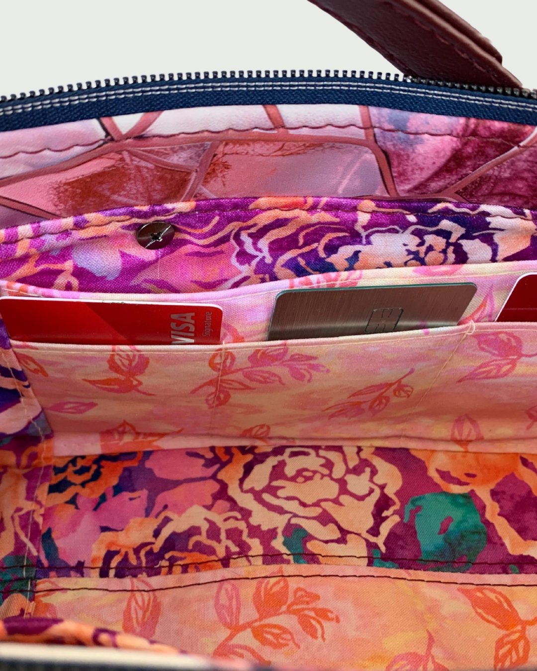 Handmade East-West style bag interior which is made of cotton woven in two floral prints of pink, purple and green. A combination of a slip pocket and a three-cardslot panel is sewn into the side. 3 credit cards are placed vertically in the cardslots. The top zipper is navy tape with gunmetal teeth. 