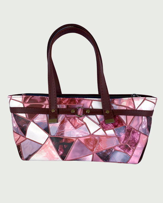 Handmade East-West style bag made from vinyl in a print of fracture glass in colors of pink, rose, maroon, and blue. Two handles made from maroon marine vinyl are attached, front and back, to a wrap-around strap detail that is held together with a carabiner ring in the front. All hardware is a shiny gunmetal. 