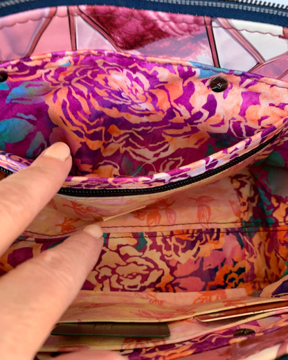 Handmade East-West style bag interior which is made of cotton woven in two floral prints of pink, purple and green. A combination of a slip pocket and a zipper pocket panel is sewn into the side. The top and the pocket zippers are navy tape with gunmetal teeth. A partial view of the other interior side of the bag is seen with a couple of cards in slots.