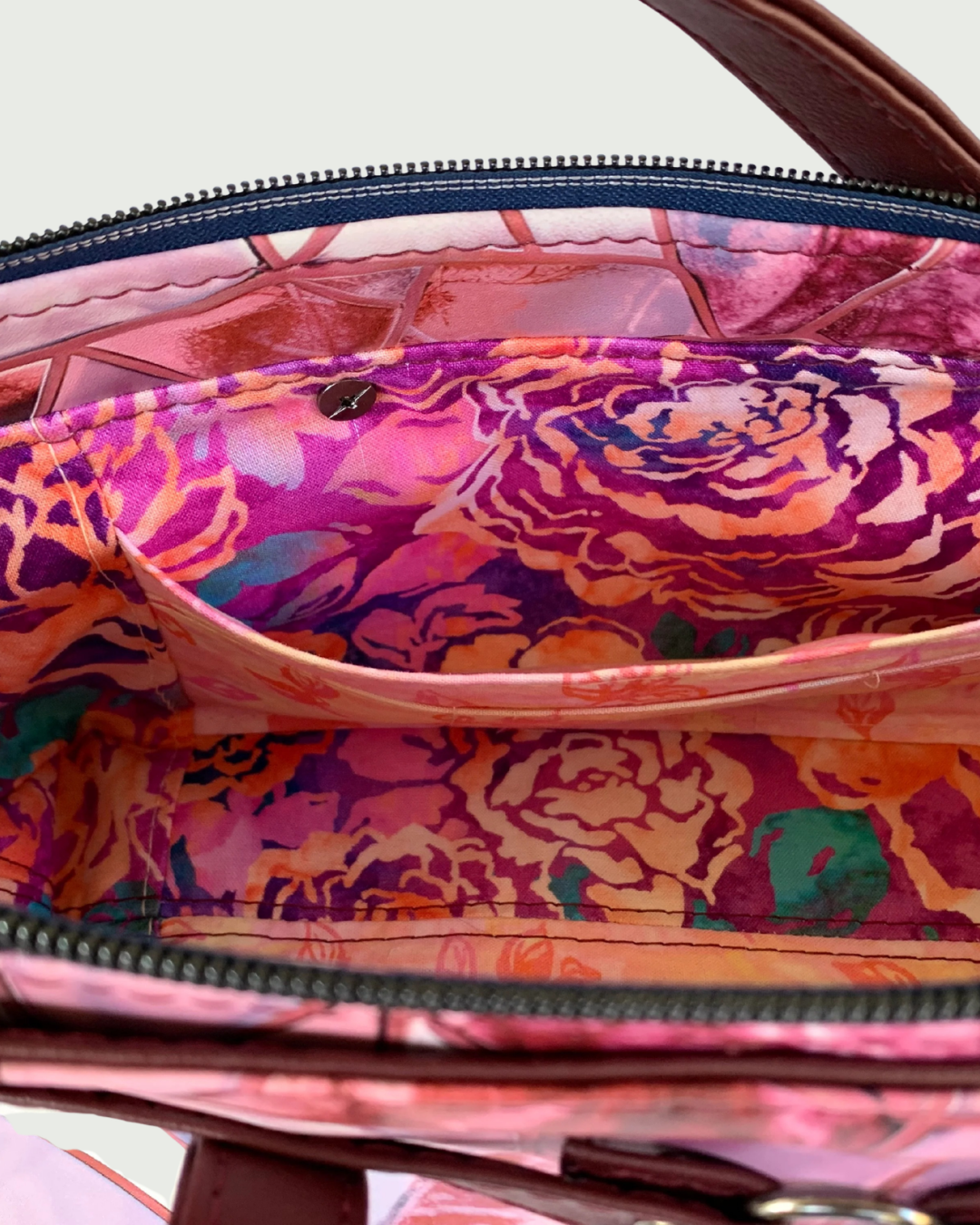 Handmade East-West style bag interior which is made of cotton woven in two floral prints of pink, purple and green. A combination of a slip pocket and a three-cardslot panel is sewn into the side. The top zipper is navy tape with gunmetal teeth. 