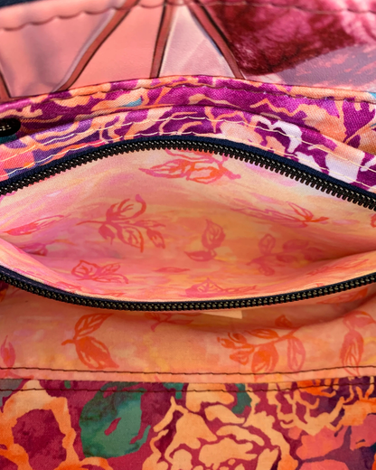Handmade East-West style bag interior which is made of cotton woven in two floral prints of pink, purple and green. A combination of a slip pocket and a zipper pocket panel is sewn into the side. The zipper is open displaying the pocket interior. The zipper is navy tape with gunmetal teeth.