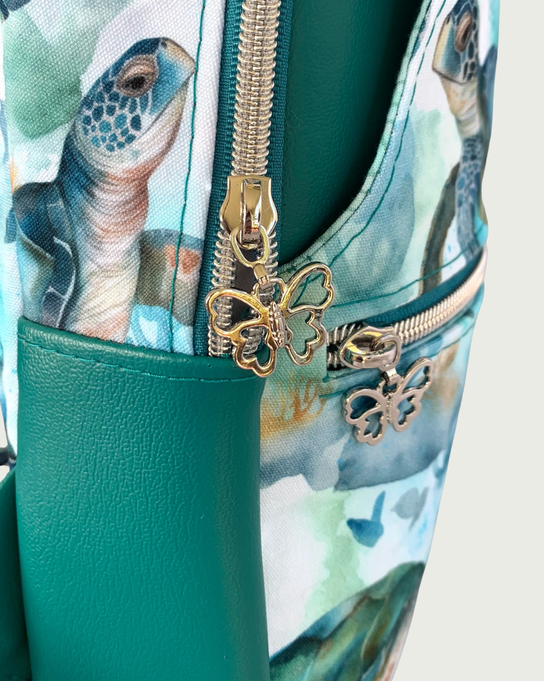 Handcrafted sling bag closeup view of water-resistant canvas with a print of sweet sea turtles in teal, aqua, green, brown, and white. The gusset and main compartment are solid teal faux leather. The hardware is all nickel including the zipper teeth on teal zipper tape and the butterfly zipper pulls.