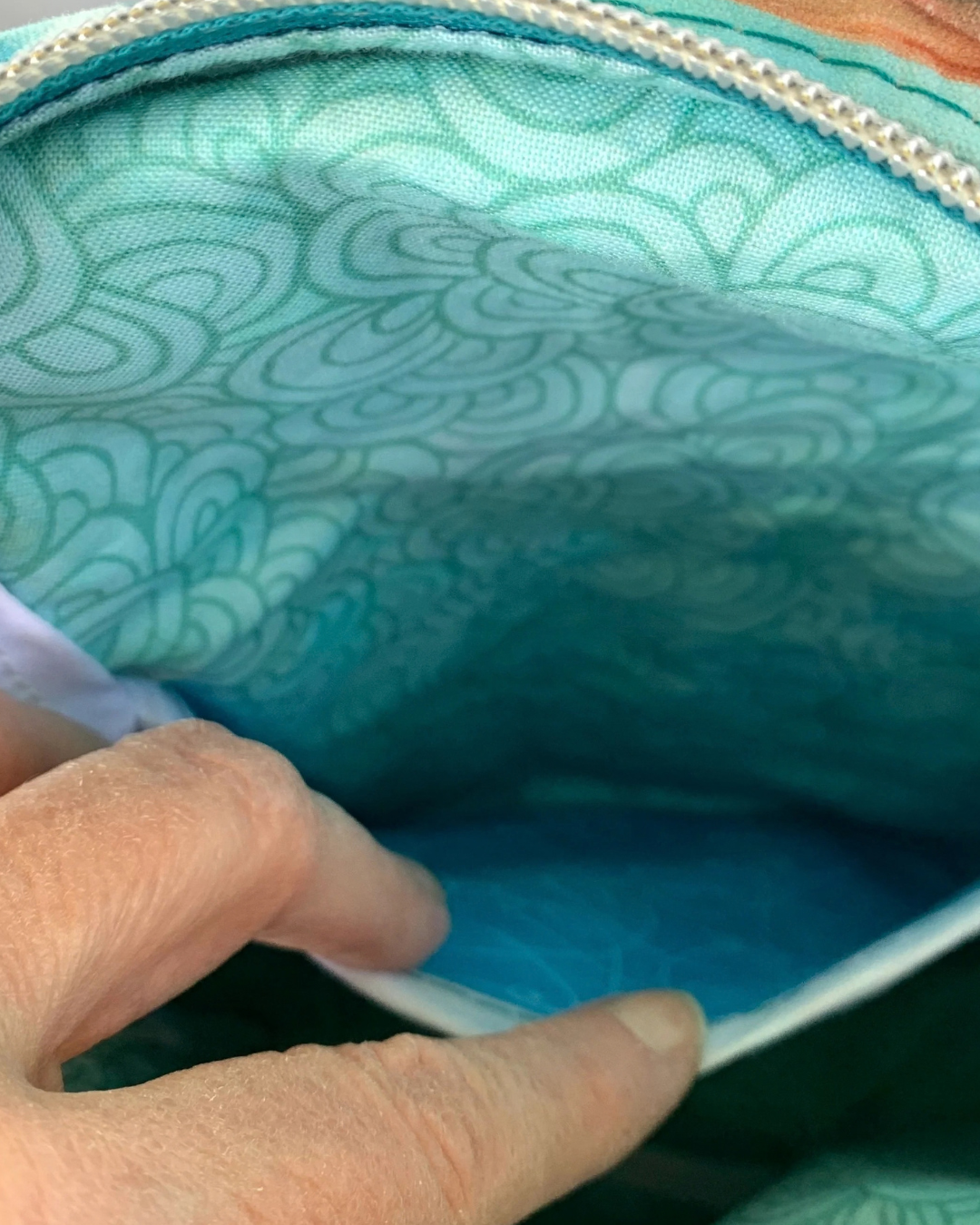 Handcrafted sling bag made of water-resistant canvas. A hand is holding open the interior slip pocket revealing aqua cotton lining.