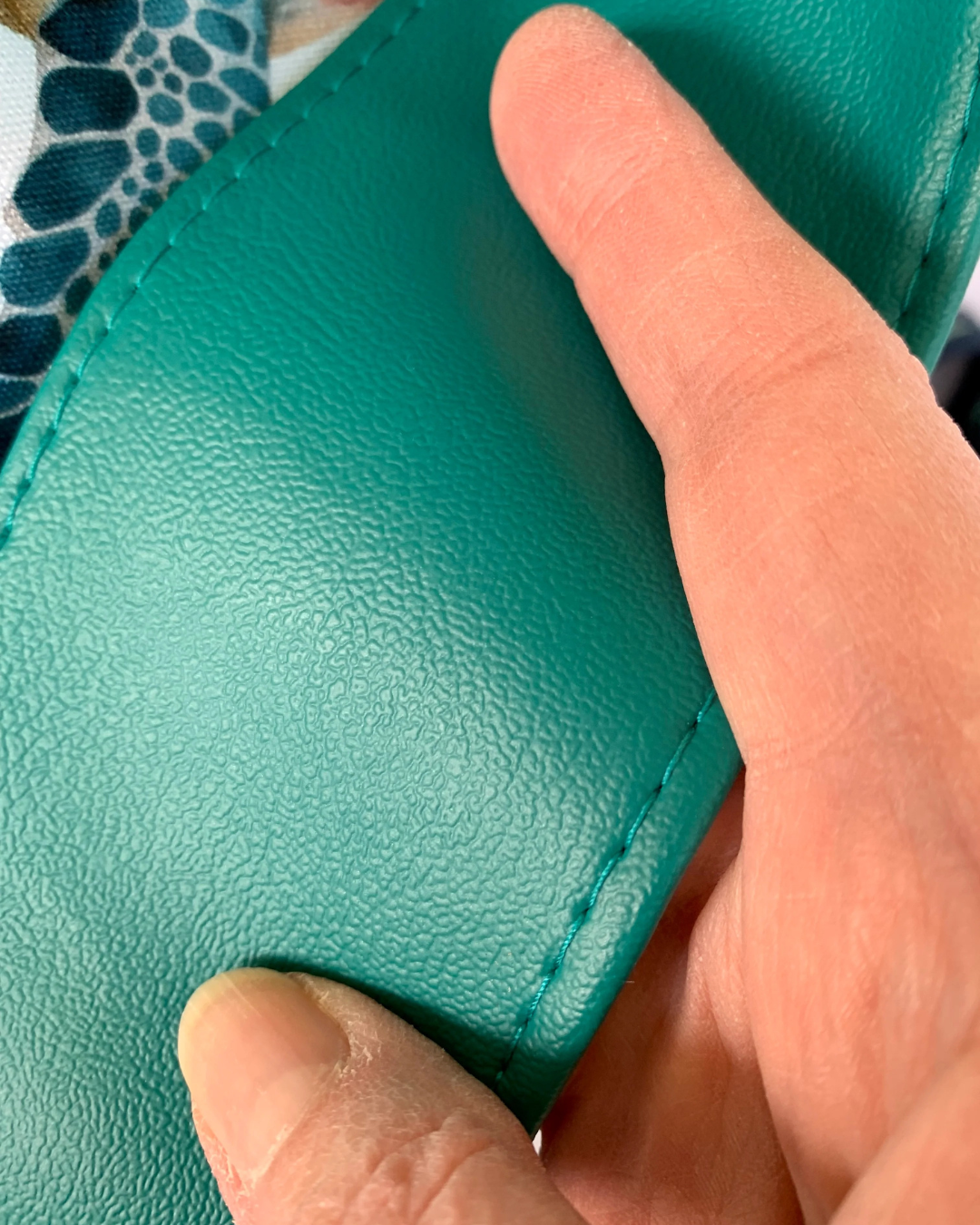 A close up view of a hand holding a wide teal faux leather shoulder strap from a handmade sling bag.