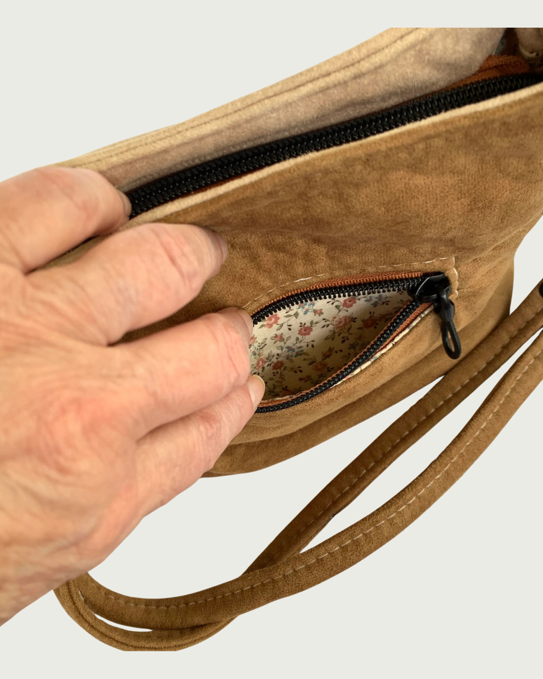 A brown faux suede handbag zoomed in to see the inside of the exterior zippered pocket.