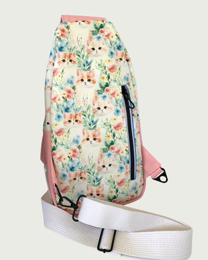 The back side of a handcrafted sling bag with vintage kitty faces featuring pink faux leather accents with an adjustable wide white cotton webbing strap also repositional for left and right handed wear. All hardware is matte black including the vertical zipper teeth on white zipper tape.