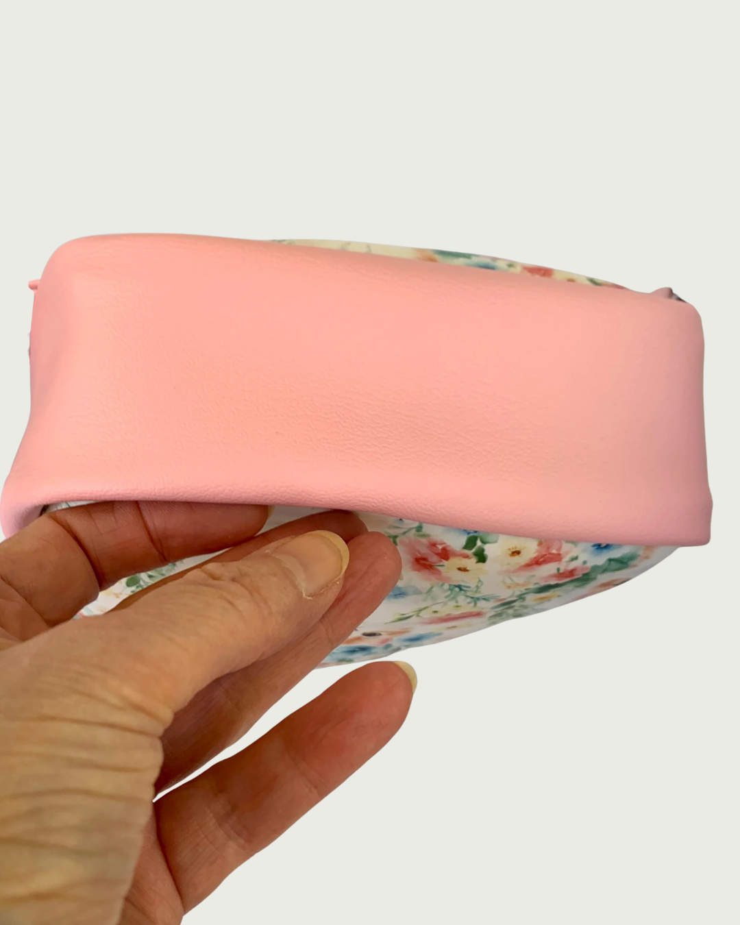The pink vinyl bottom gusset of a handcrafted sling bag with vintage kitty faces held up by a hand.