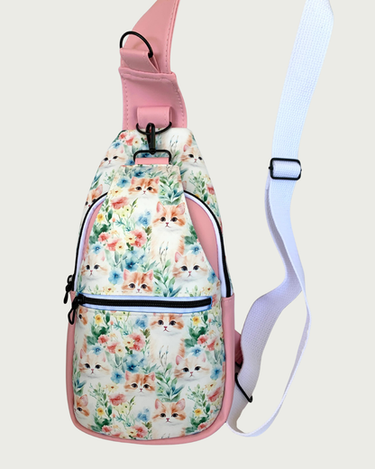 Handcrafted Sling bag with vintage kitty faces featuring pink faux leather accents with an adjustable wide white cotton webbing strap also repositional for left and right handed wear. All hardware is matte black including the zipper teeth on white zipper tape. A front zipper pocket is shown as well as a front panel that unhooks with a swivel held onto a d-ring. Behind that is a curved zippered main compartment.