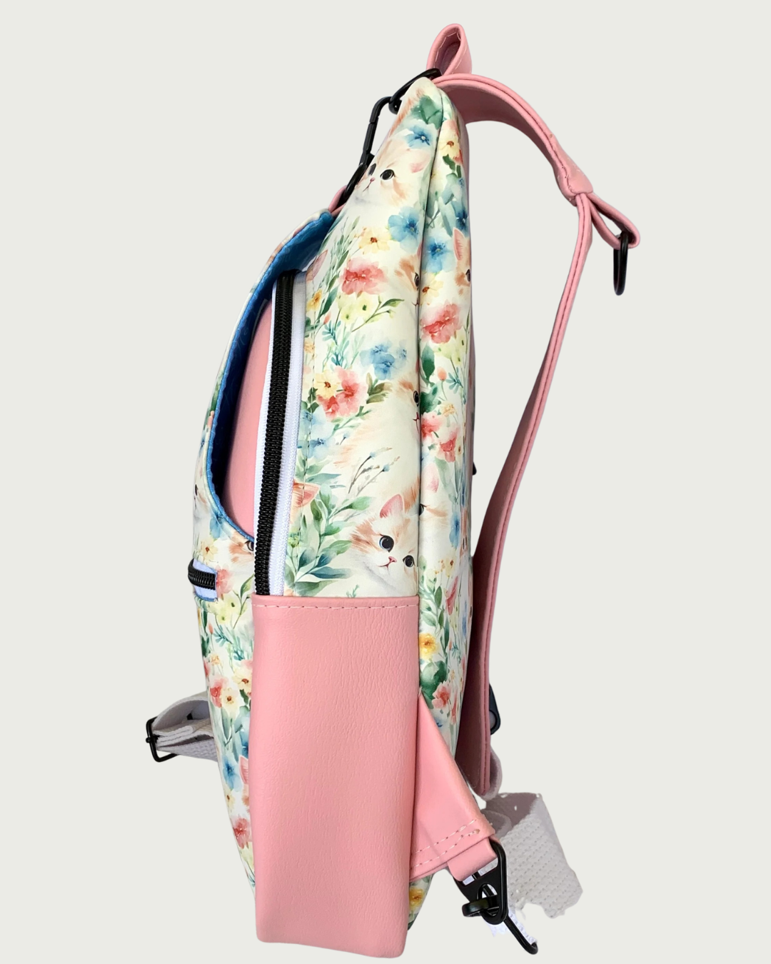 The right side view of a handcrafted sling bag with vintage kitty faces featuring pink vinyl accents including a wide shoulder strap with an adjustable white cotton webbing strap extension also repositional for left and right handed wear. All hardware is matte black including the zipper teeth on white zipper tape.