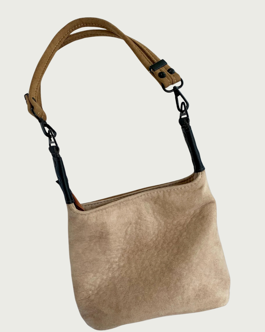 A tan faux suede purse with black faux-leather strap connectors and hardware and a brown shoulder strap.