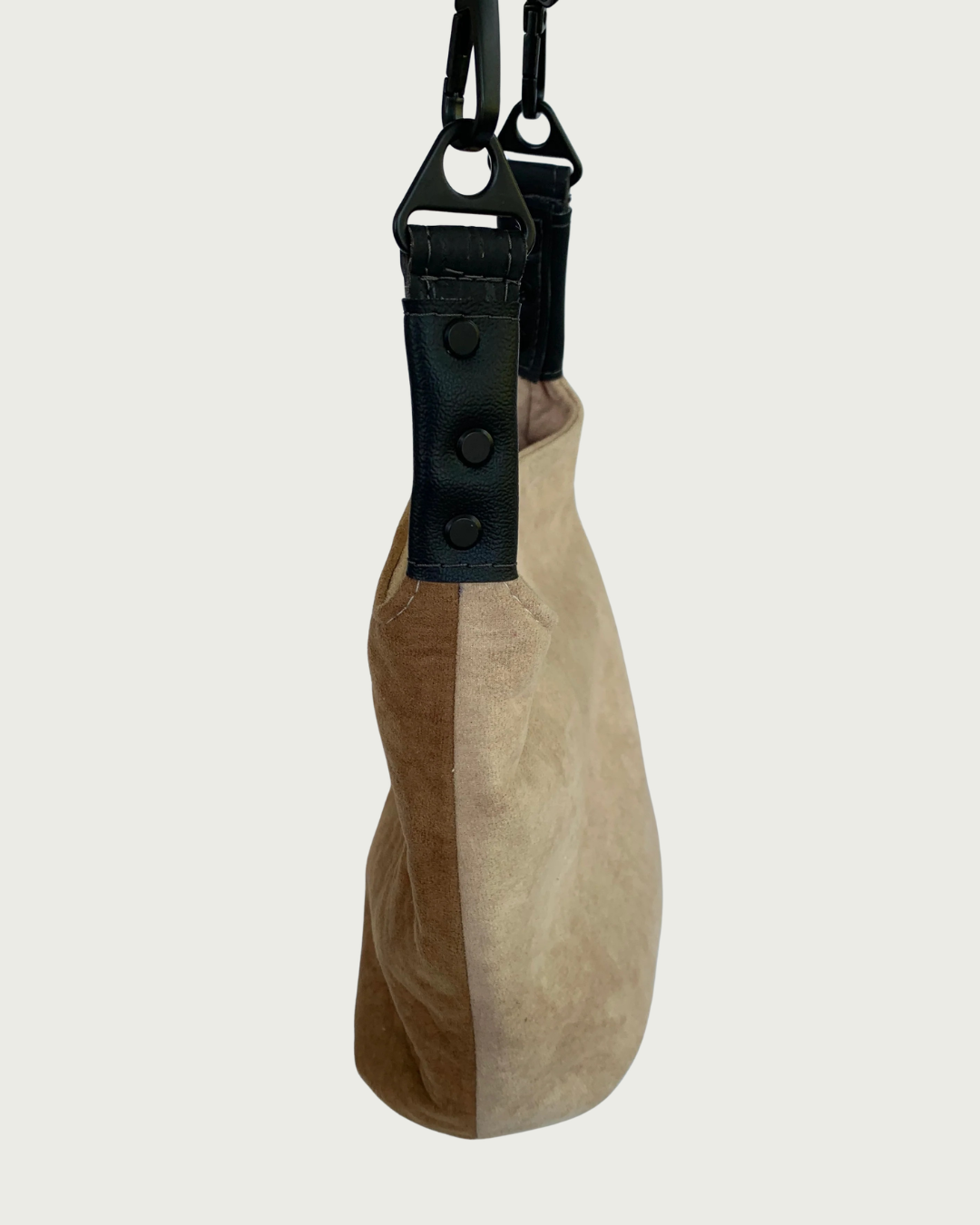 A 2-toned faux suede shoulder bag with black faux-leather strap connectors as seen from the side.
