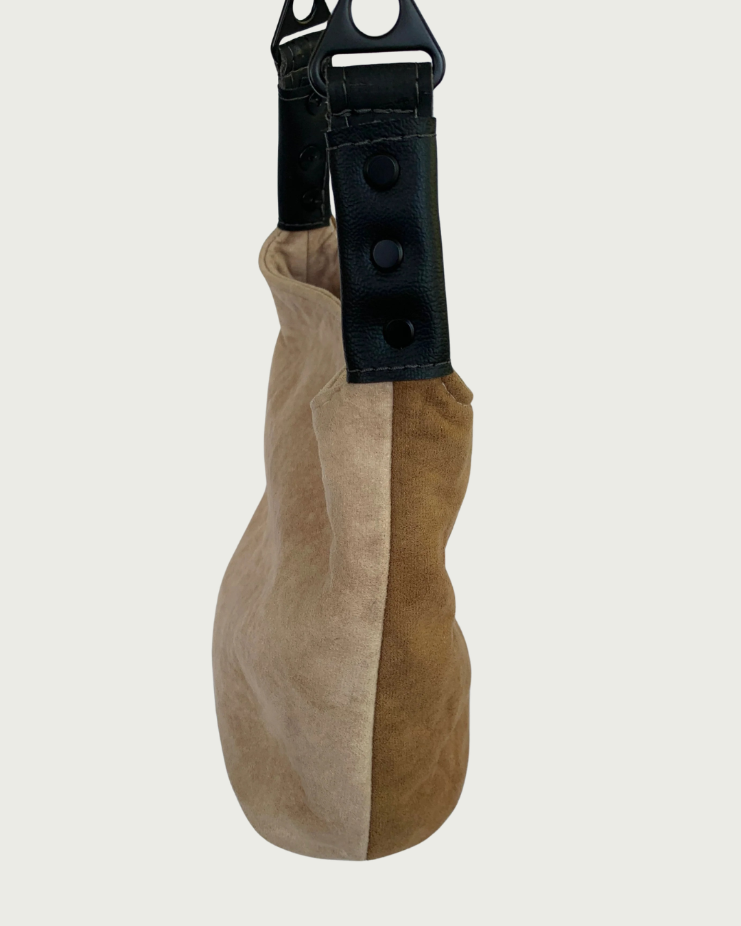 A minimalist shoulder bag made of split tan and brown suede, featuring black faux leather strap connectors and matt black hardware.