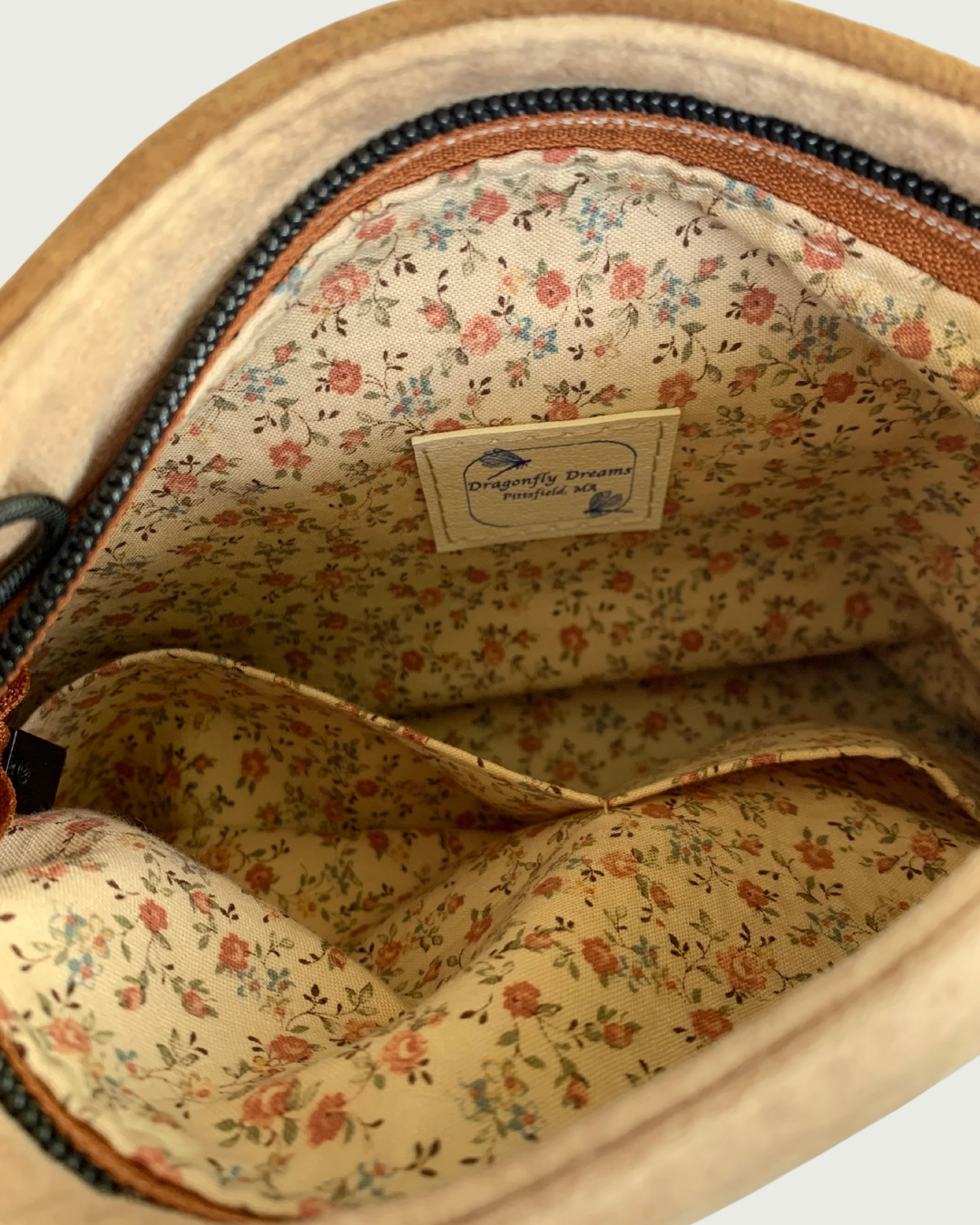 A Close-up view of the interior of a zippered purse showing the tan-colored lining with small pink flowers and 2 slip pockets.