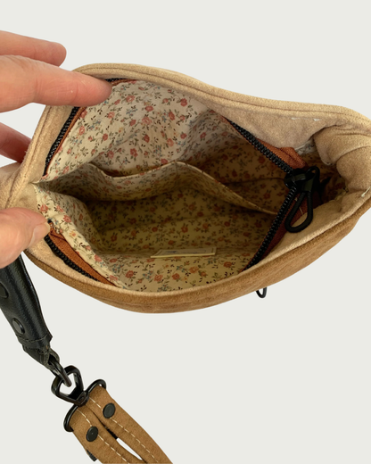 A close-up of a brown and tan faux suede  bag showing a floral-patterned interior lining with two slip pockets.