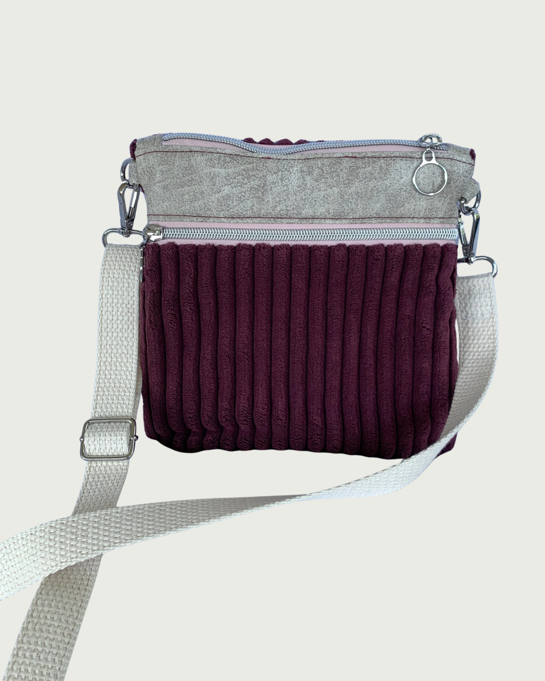 Handmade maroon wide-wale corduroy crossbody bag with sand-colored distressed vinyl accents. Attached is an adjustable and detachable cotton webbing, natural colored strap. Nickel hardware throughout. There is a pocket with pink zipper tape. 