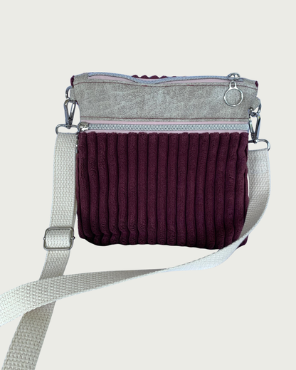 Handmade maroon wide-wale corduroy crossbody bag with sand-colored distressed vinyl accents. Attached is an adjustable and detachable cotton webbing, natural colored strap. Nickel hardware throughout. There is a pocket with pink zipper tape. 