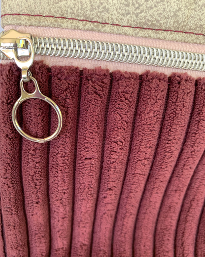 Closeup view of a handmade maroon wide-wale corduroy crossbody bag with sand-colored distressed vinyl accents. Pink zippered pocket with nickel teeth and circle zipper pull.
