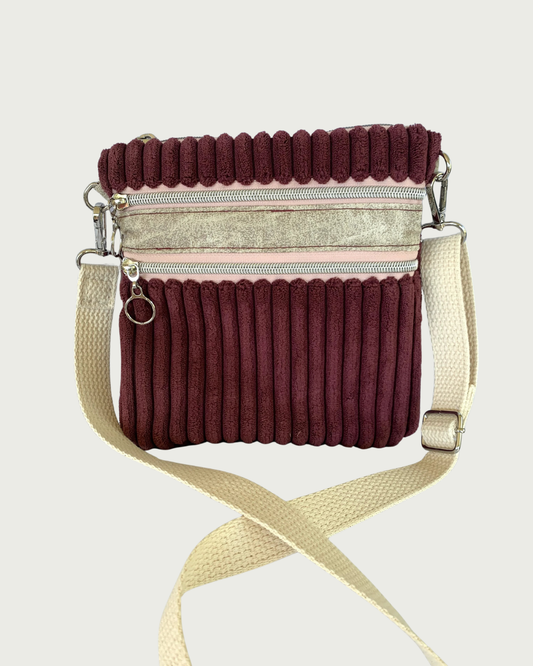Handmade maroon wide-wale corduroy crossbody bag with sand-colored distressed vinyl accents. Attached is an adjustable and detachable cotton webbing, natural colored strap. Nickel hardware throughout. There are two pockets with pink zipper tape. 
