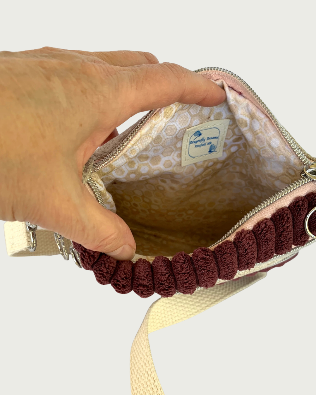 Top view of opened handmade maroon wide-wale crossbody bag showing a lining of tan, gold, and white geometric print with a Dragonfly Dreams label sewn in.