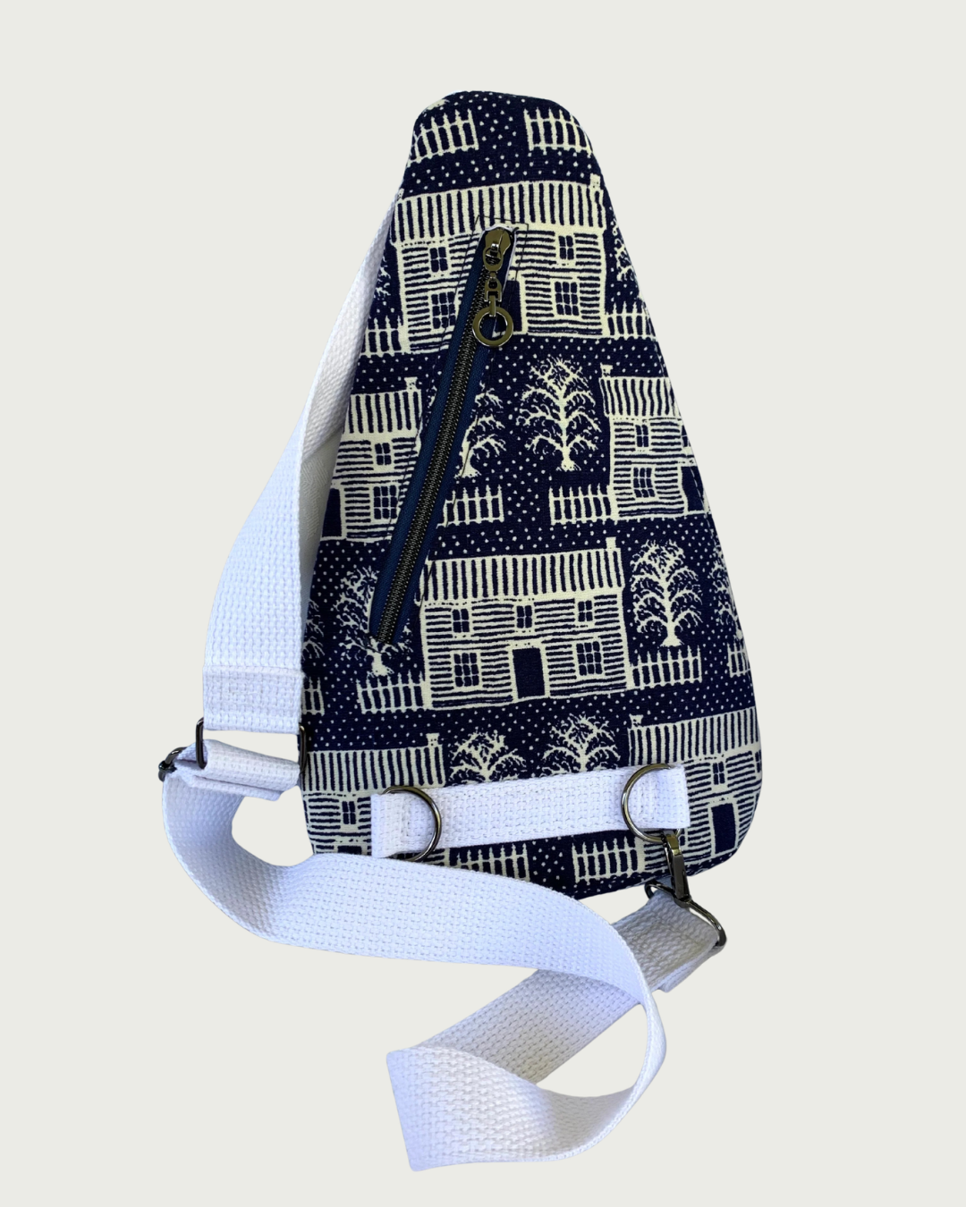 Handmade navy and off-white houses and picket fences crossbody sling bag with white cotton webbing strap adjustable in length and also for left and right carry by switching lobster clasp from one d-ring to another. Gunmetal hardware throughout, and a navy zipper running up and down.