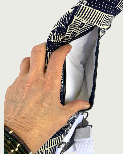 Handmade navy and off-white houses and picket fences crossbody sling bag with a hand holding open the back navy zippered pocket. The lining is white as is the adjustable cotton webbing strap with gunmetal hardware throughout.