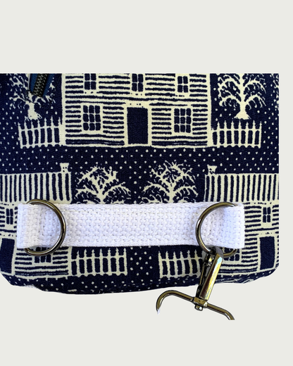 Handcrafted navy crossbody sling bag with off-white houses closeup of sewn-in cotton webbing strap securing 2 d-rings. The gunmetal swivel clasp from an adjustable strap is attached to one d-ring.