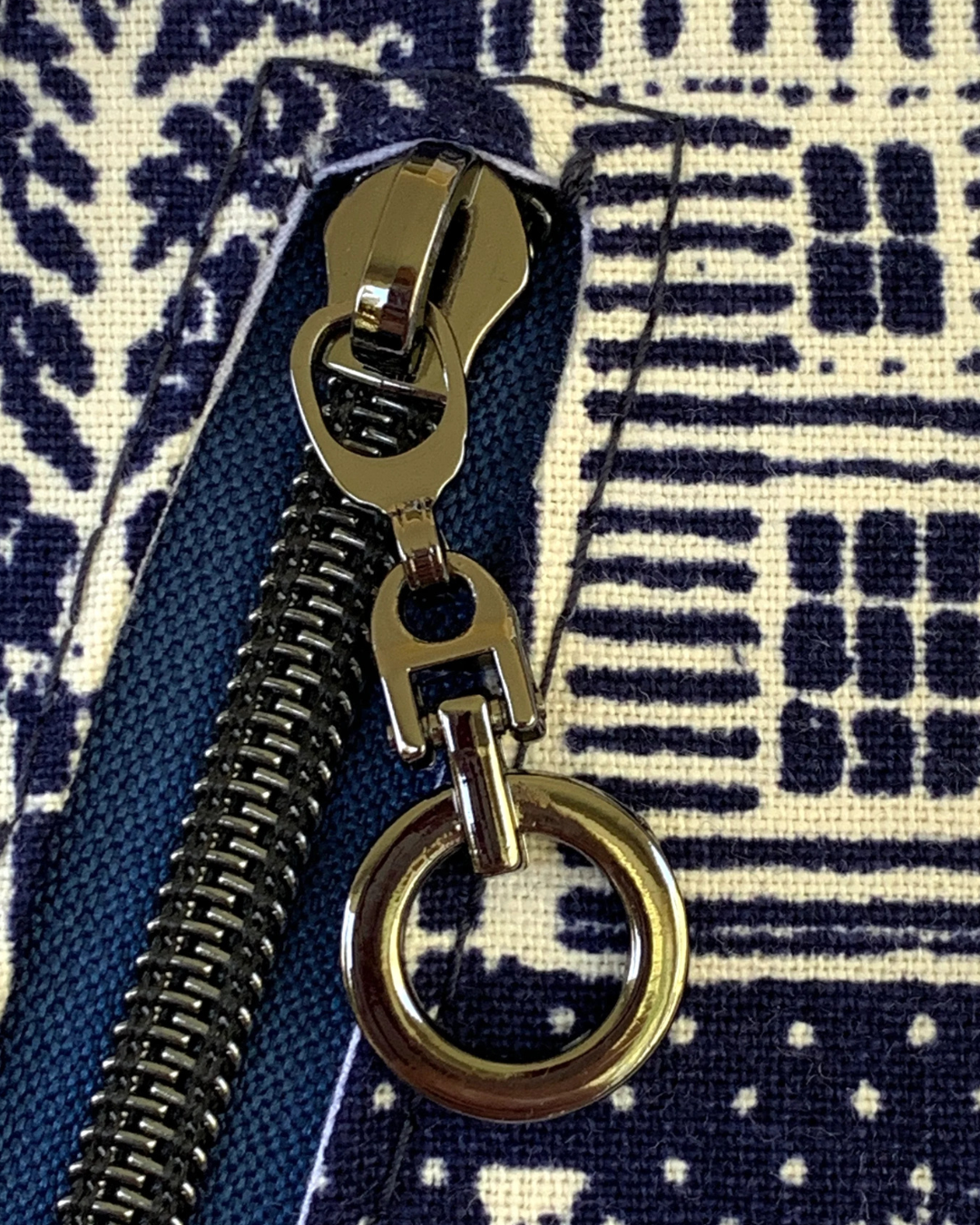 Close up of zipper on handcrafted crossbody sling bag of navy and off-white. The zipper tape is navy blue and the zipper teeth and dangling ring zipper pull are gunmetal.