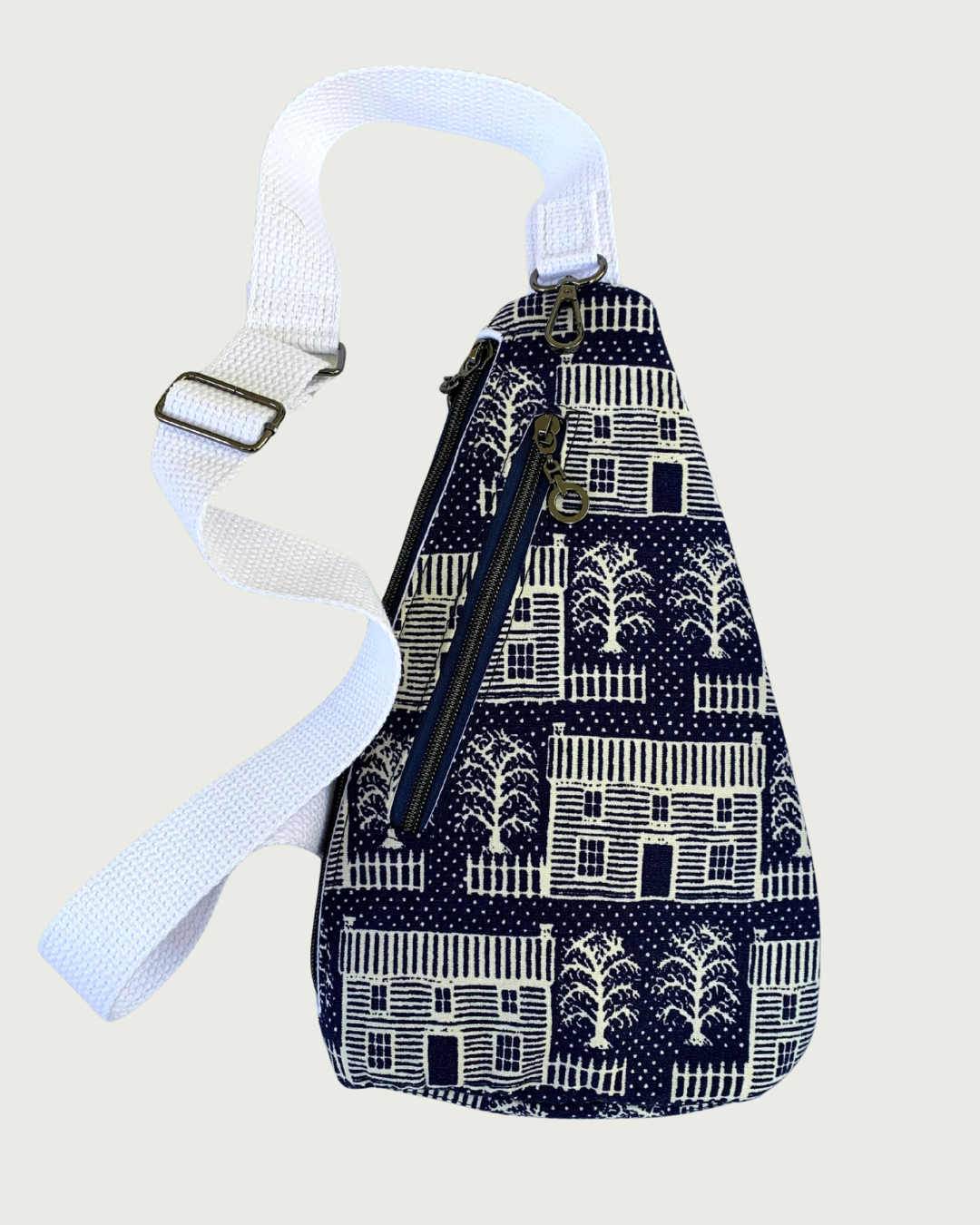 Handmade navy and off-white houses and picket fences crossbody sling bag with adjustable white cotton webbing strap, gunmetal hardware, and a navy zipper running up and down.