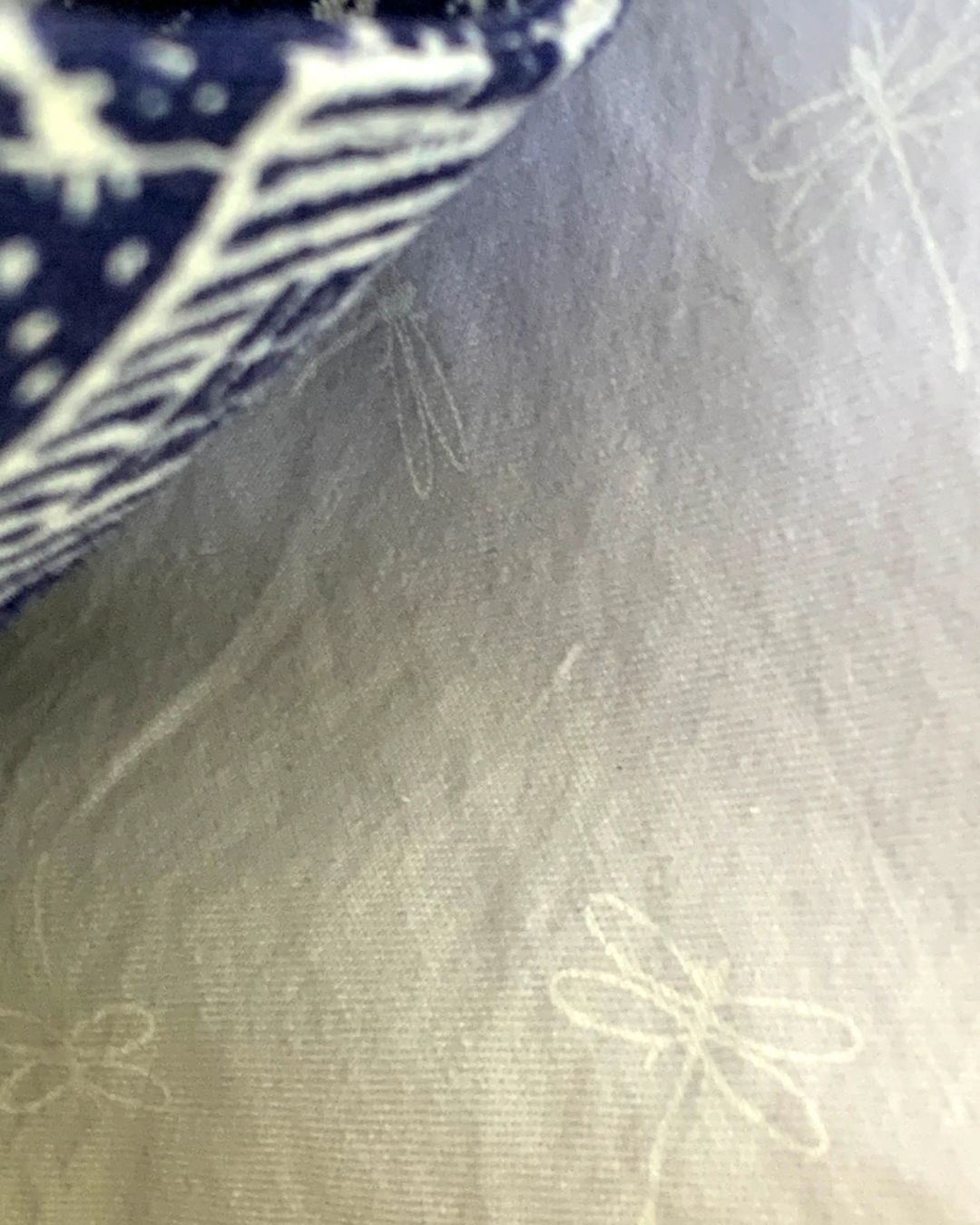 Handmade crossbody sling bag interior lining of white dragonflies on white cotton fabric background. Part of the slip pocket made from off-white houses and picket fences on navy background can be seen.