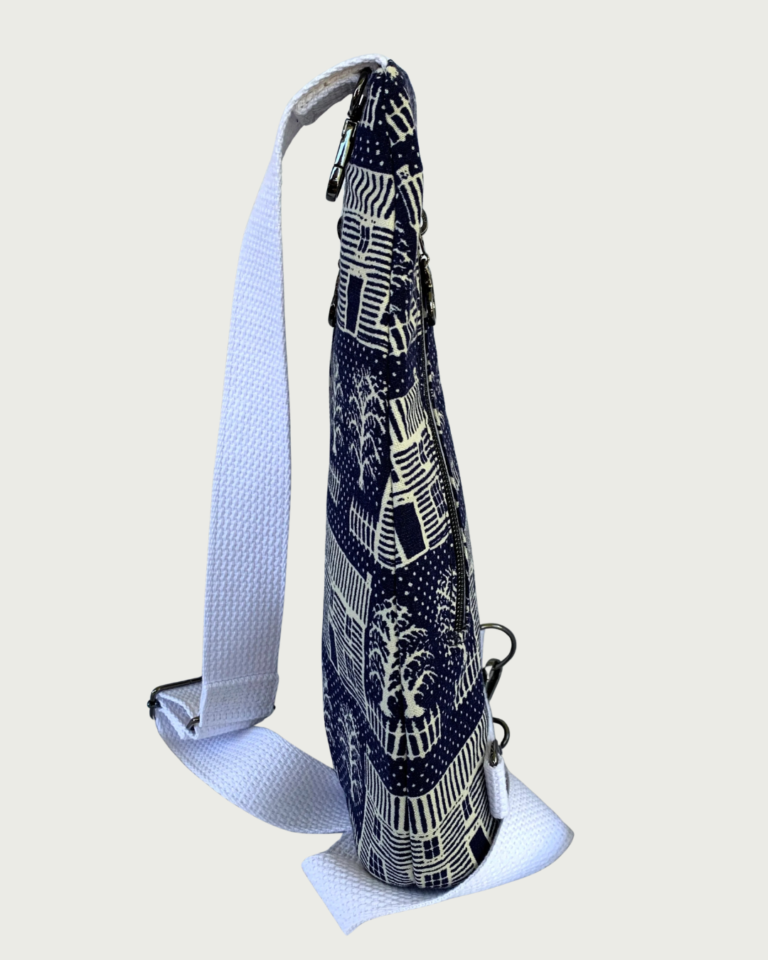 Side view of Handmade navy and off-white houses and picket fences crossbody sling bag with white cotton webbing adjustable strap and gunmetal hardware.