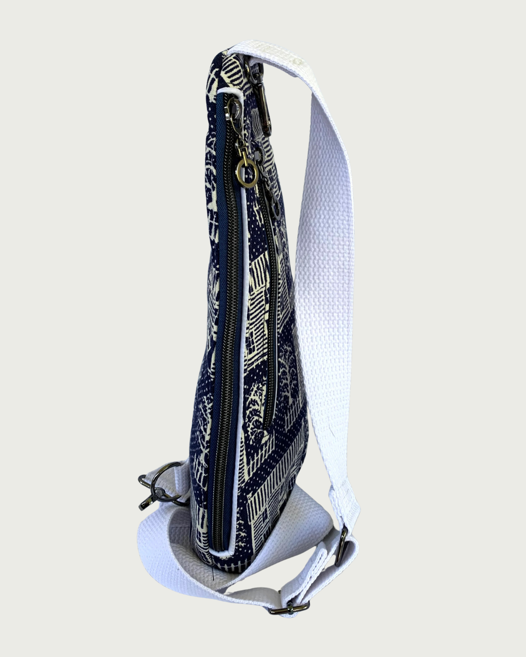 Handmade navy and off-white houses and picket fences crossbody sling bag showing side view main closure by a navy zipper running the length of the bag with gunmetal hardware and white cotton webbing adjustable strap.