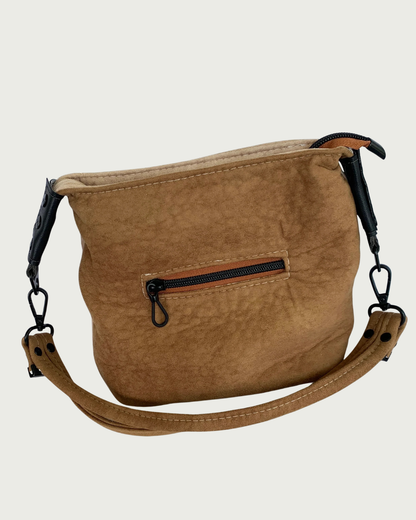 A brown suede shoulder bag with a brown  strap, matt black hardware, and small zippered pocket.